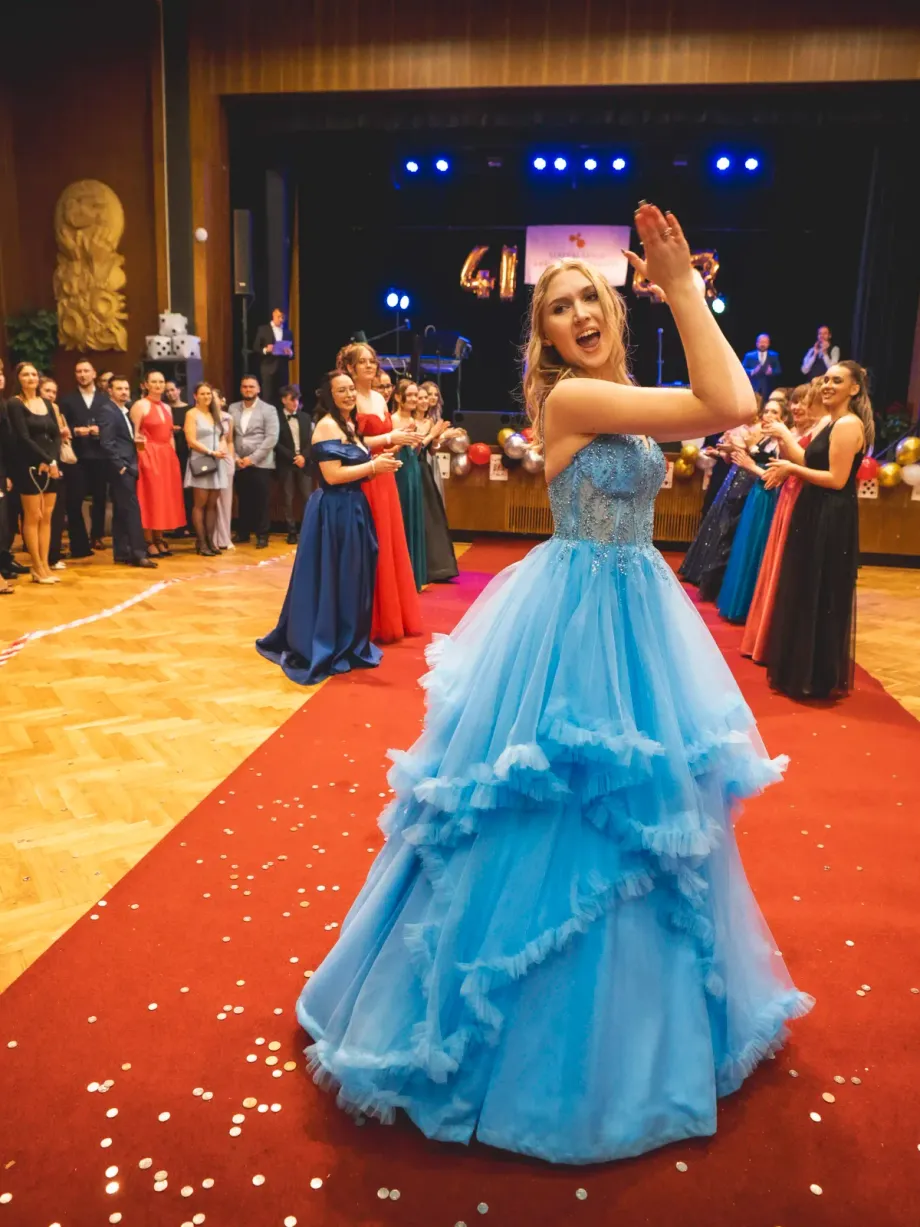 Maturantka v plesových šatech při nástupu na červený koberec