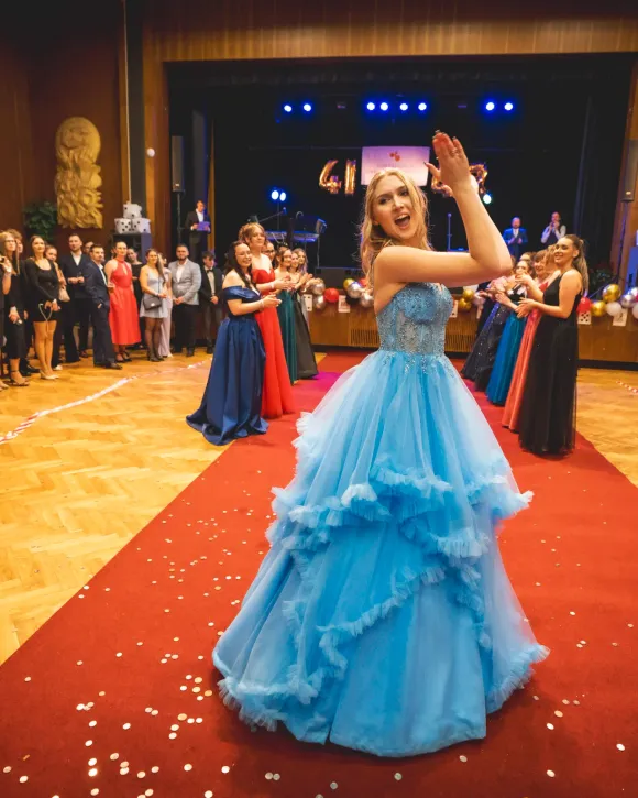 Maturantka v plesových šatech při nástupu na červený koberec